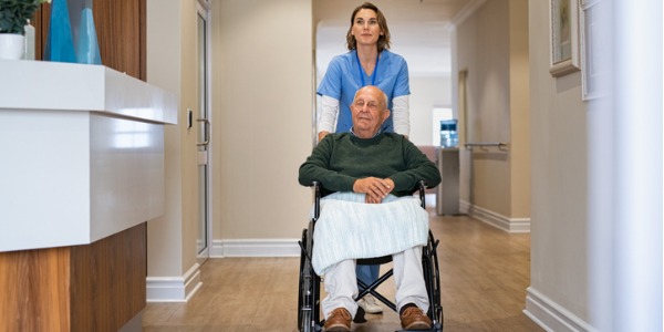 A certified nursing assistant pushing a senior man in a wheelchair.