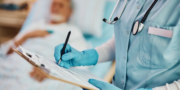 A critical care nurse documenting a patient's vitals in a hospital room.