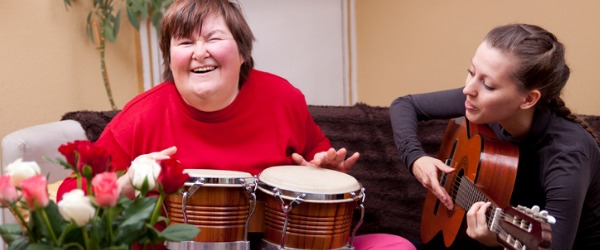 A music therapist playing a guitar while her client plays the bongo drums.