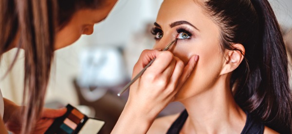 A makeup artist applying eye liner to a model's eye.