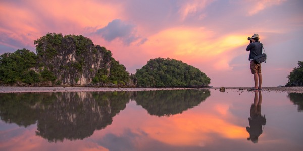 A photographer taking a picture of a beautiful sunset and beach.