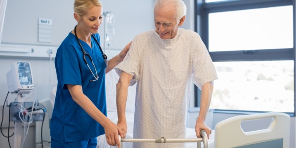 A rehabilitation nurse helping an older patient get out of his hospital bed.