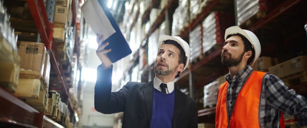 A supply chain manager talking to a worker in a warehouse.
